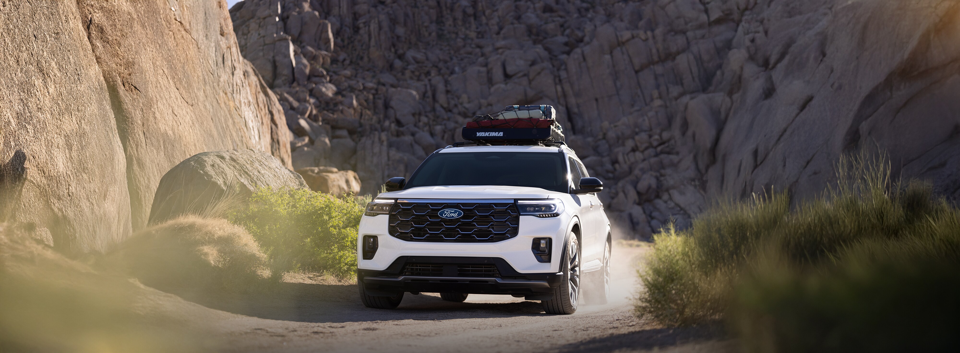 Una SUV Ford Explorer® Platinum™ 2027 con equipaje en el techo, levantando polvo mientras pasa por un cañón de tierra