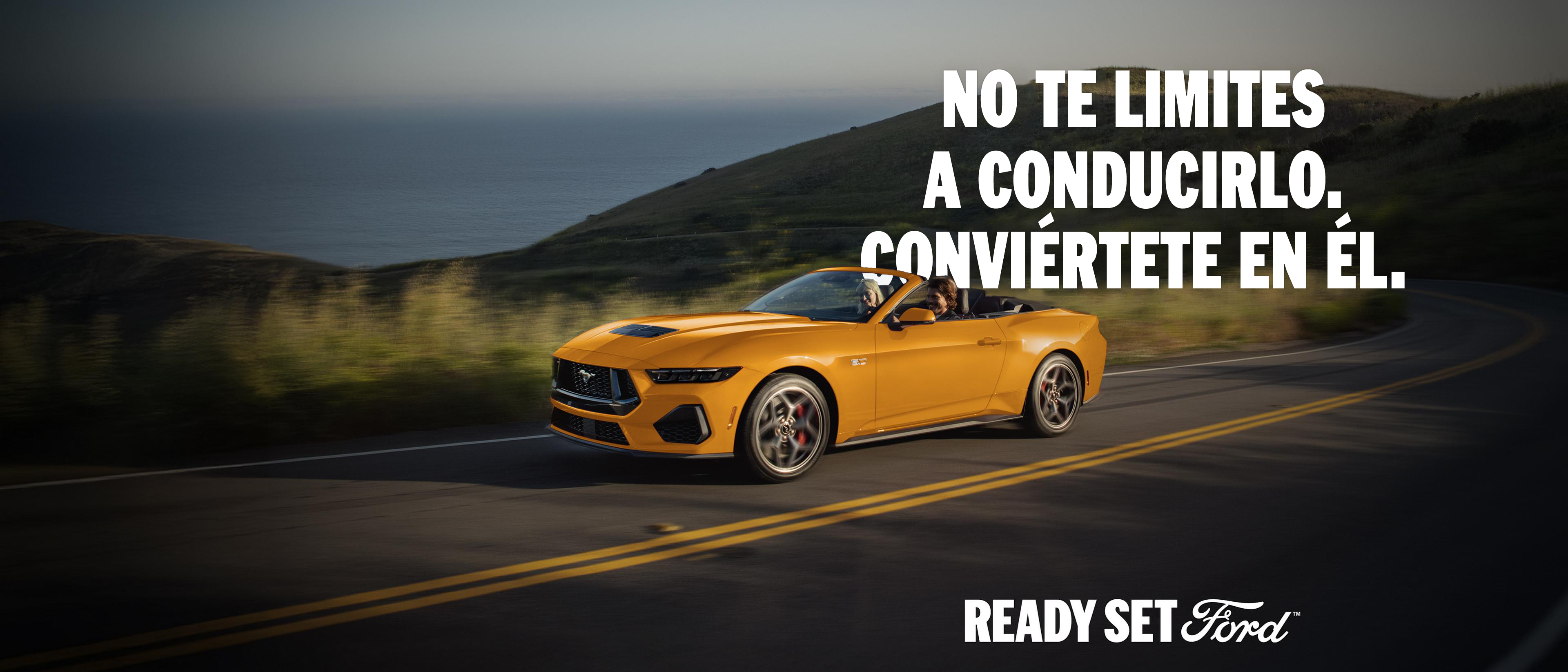 Dos personas en un Ford Mustang® GT Convertible 2026 en Orange Fury Metallic Tri-Coat andando por una carretera costera