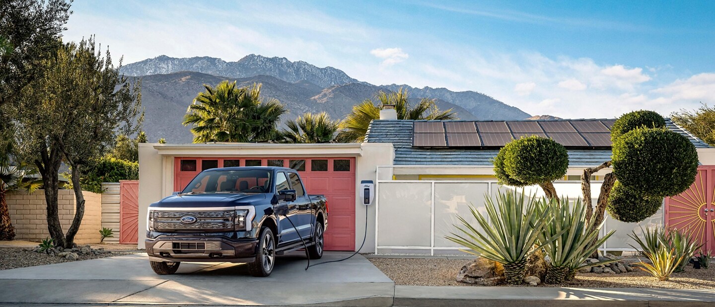 Una Ford F-150® Lightning® 2023 black estacionada en la entrada de una casa de un suburbio. El paisaje se siente árido, casi como el desierto