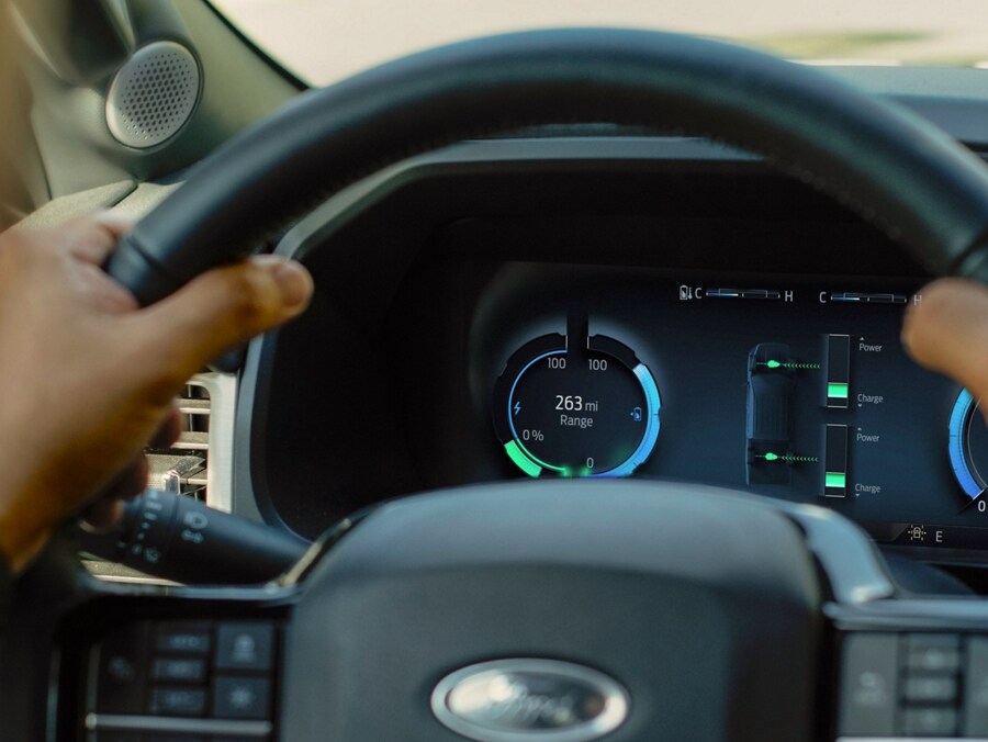Conductor de una Ford F-150® Lightning® 2023 con las manos en el volante En el grupo de instrumentos, un indicador de nivel de batería