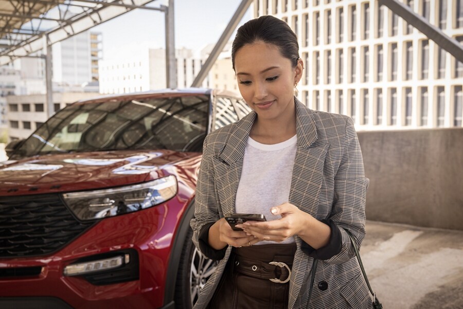 Una mujer mirando su iPhone mientras pasa caminando al lado de una SUV Ford Explorer.