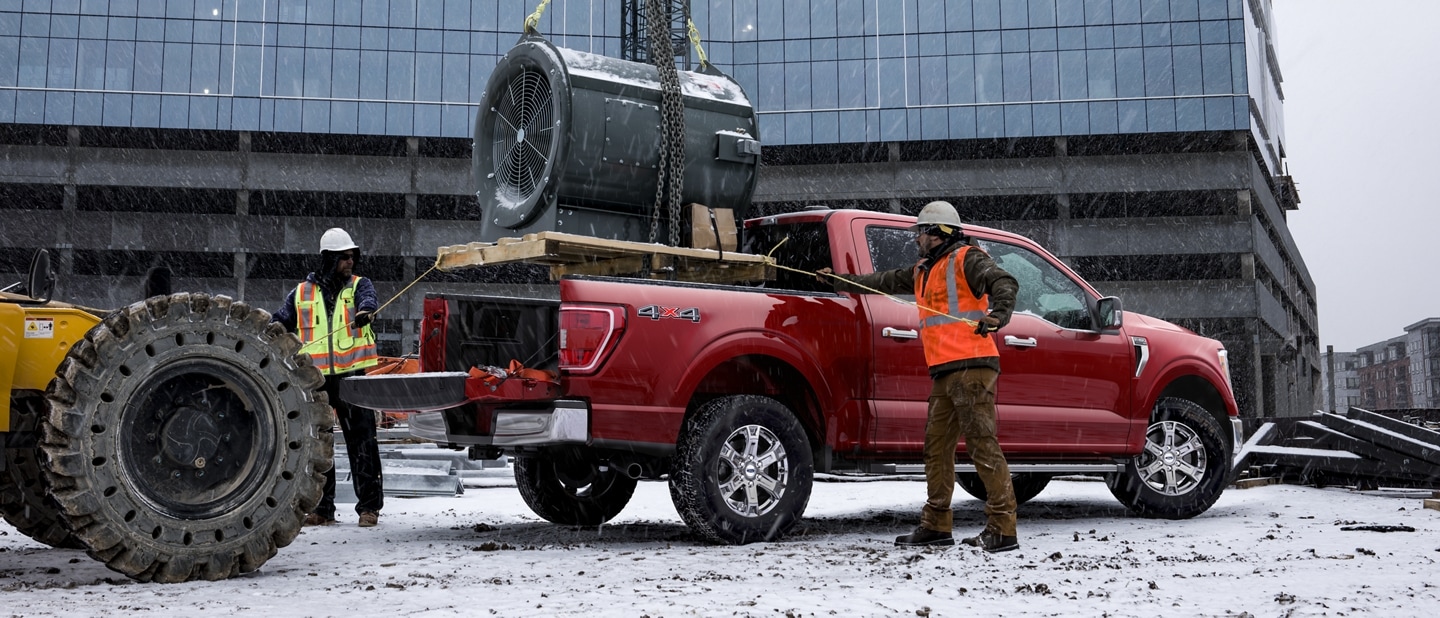 Trabajadores de la construcción cargando el motor de una turbina grande en la plataforma de una Ford F-150® XLT SuperCrew® 2022 en Race Red