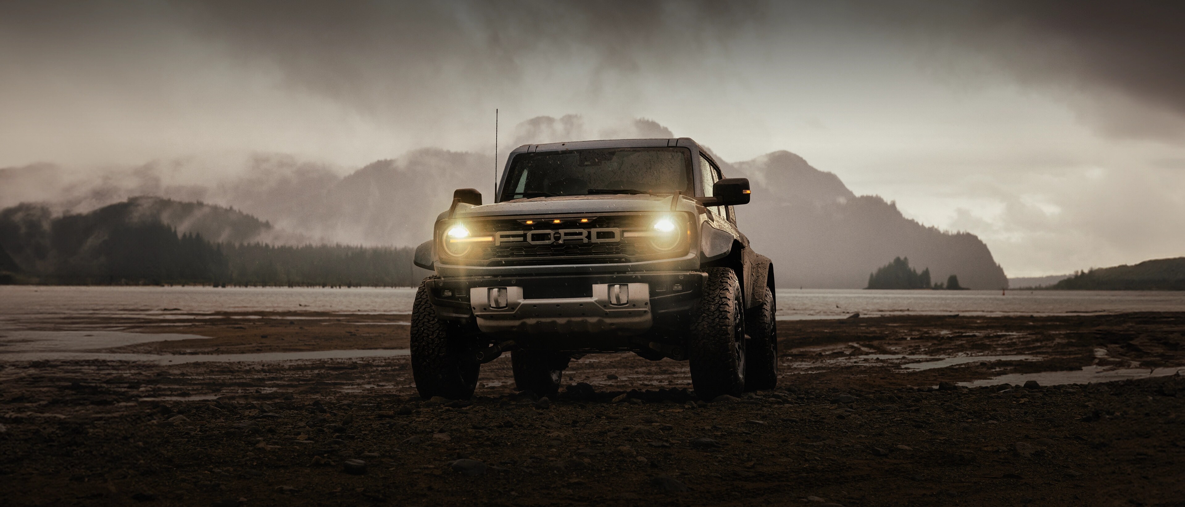 Una SUV Ford Bronco® 2025 en un lodazal cerca de una montaña nevada, con nubes de lluvia amenazando