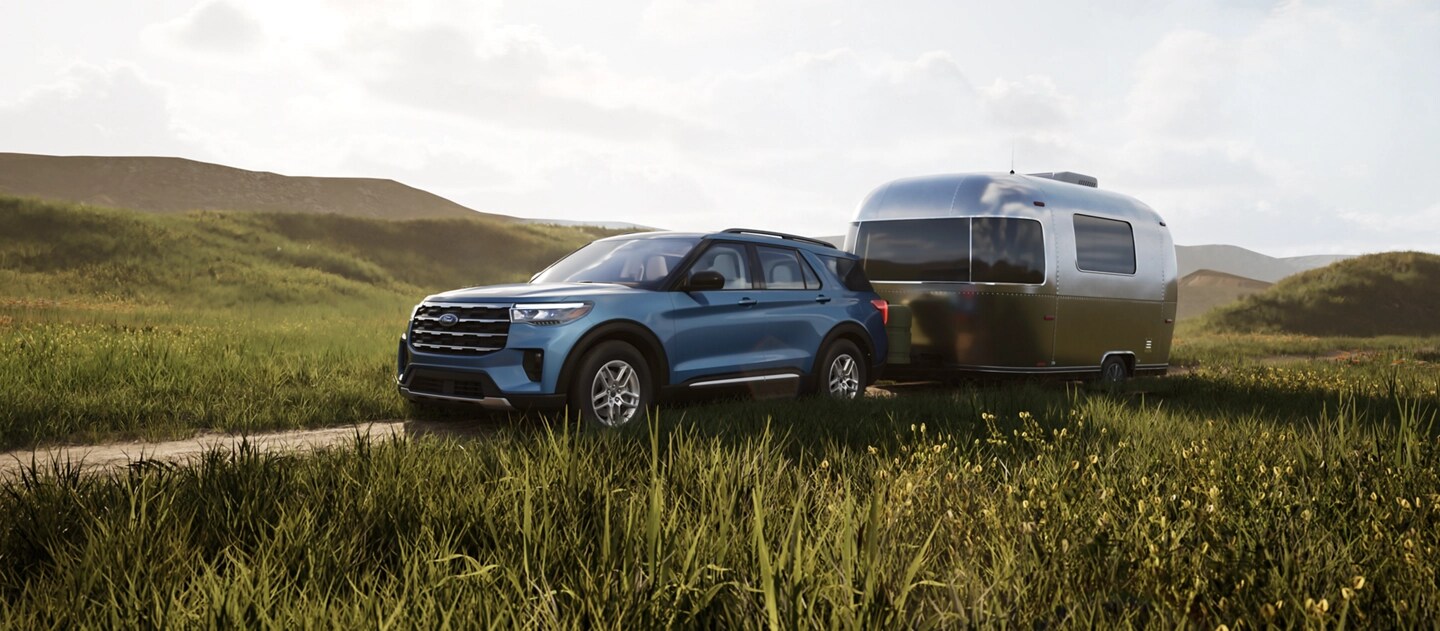 Una SUV Ford Explorer® 2025 remolca una caravana en un camino junto a un campo