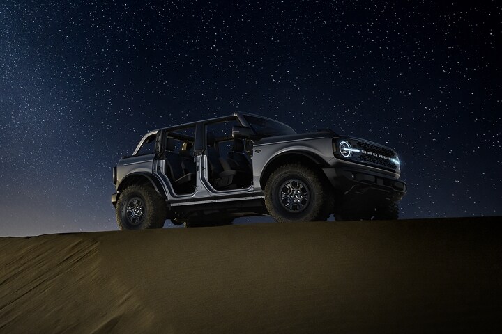 Una Ford Bronco® Wildtrak® 2024 de cuatro puertas en Iconic Silver sin puertas ni techo estacionada de noche