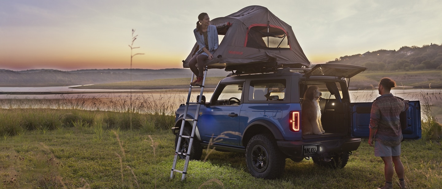 Una Ford Bronco® Badlands® 2024 en Velocity Blue con una carpa en el techo y dos caravanas