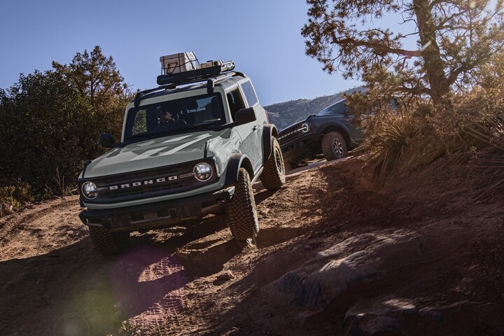 Una Ford Bronco® Black Diamond™ 2024 de dos puertas en Cactus Gray circulando por un camino con una Bronco® detrás