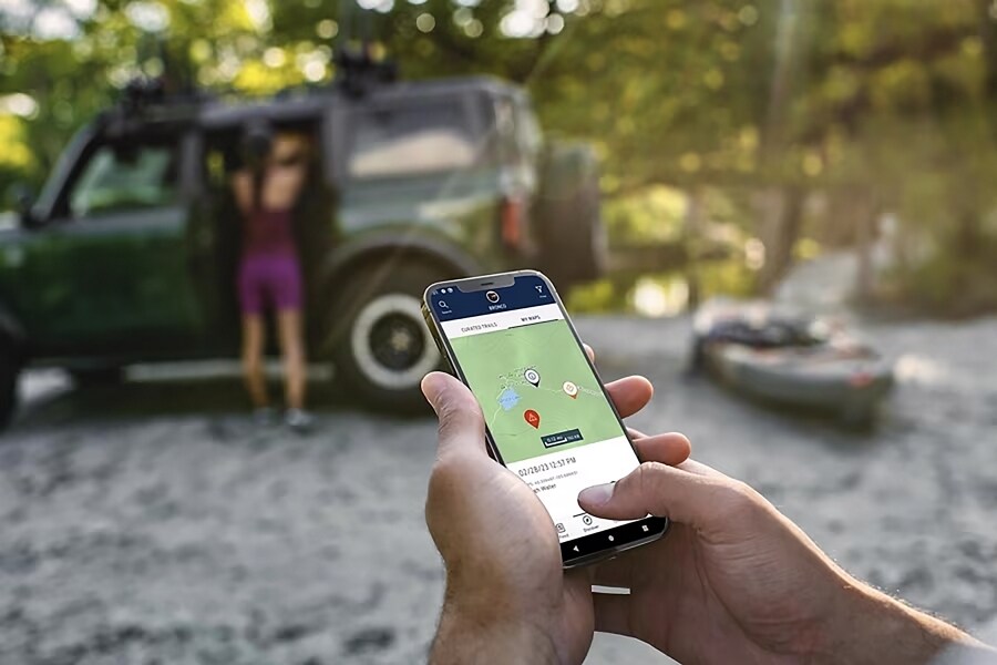 Primer plano de un smartphone que muestra los caminos con una Ford Bronco® 2024 en segundo plano