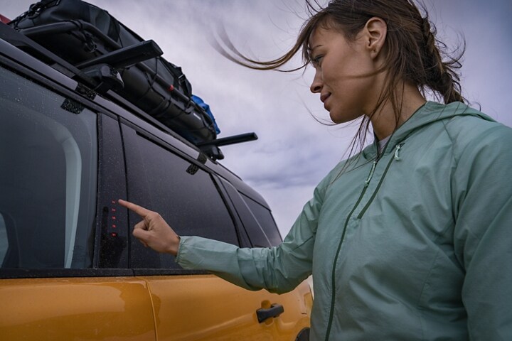 Una mujer oprimiendo el teclado mientras está parada afuera de su SUV Ford Bronco® Sport 2023