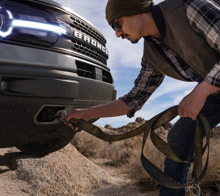 Un modelo Ford Bronco® Sport 2023 con un hombre enganchando una correa en los ganchos delanteros para remolque