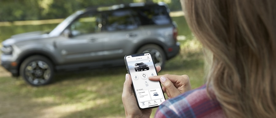 Una mujer sosteniendo un smartphone usa su Aplicación FordPass® para arrancar a distancia su SUV Ford Bronco® Sport 2023