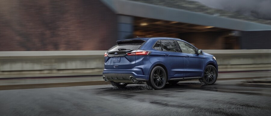 Una Ford Edge® ST-Line 2024 en Stone Blue andando por una carretera con un paso elevado de fondo