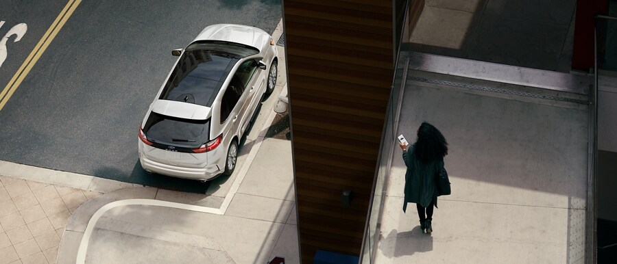 Mujer sosteniendo un smartphone en una pasarela peatonal mirando su SUV Ford Edge® 2024 estacionada en la calle abajo