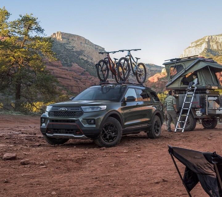 Una SUV Ford Explorer® Timberline® 2023 en Forged Green Metallic estacionada en el desierto con una carpa en la parte superior de un remolque y una familia