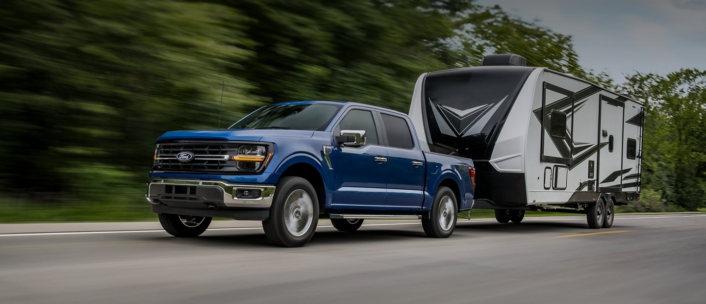 Una Ford F-150® XLT 2025 andando por un camino pavimentado con una caravana enganchada