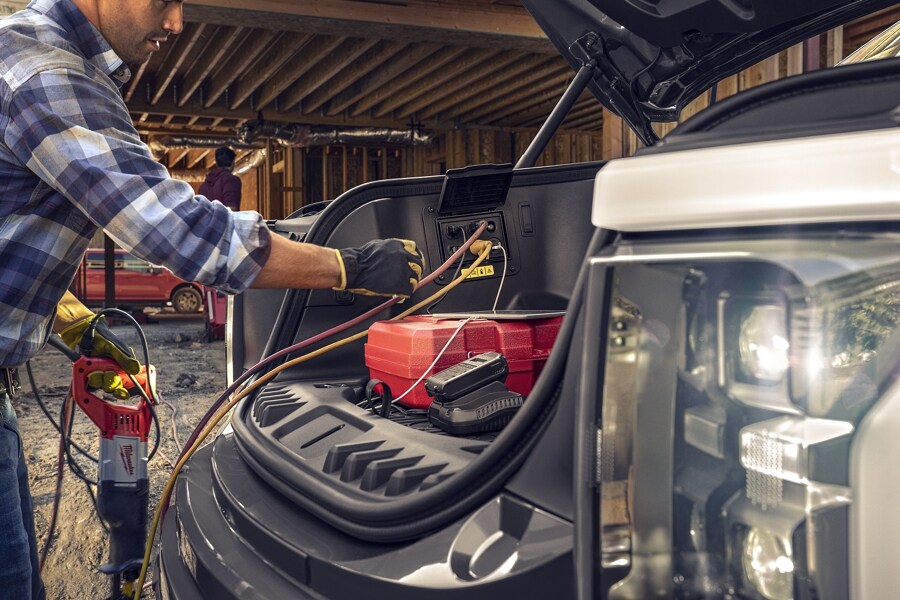 Primer plano de un hombre enchufando los cables eléctricos a los tomacorrientes de la Cajuela Delantera Mega Eléctrica