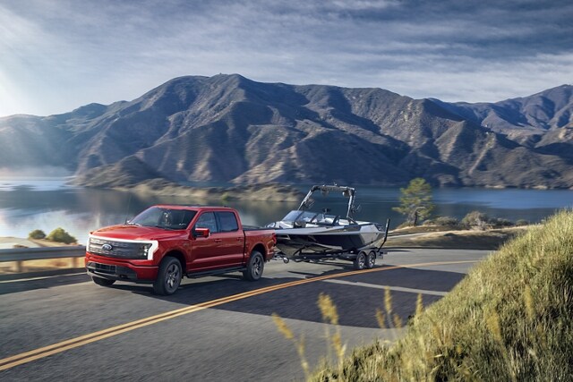 Una Ford F-150 Lightning® 2023 remolcando un bote por un camino montañoso y montañas en segundo plano