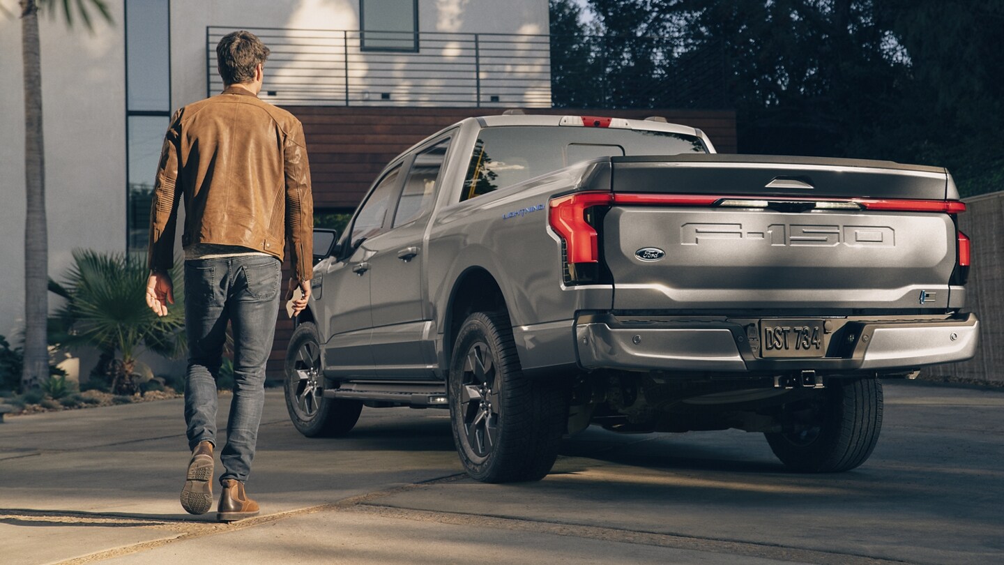 Vista trasera de una Ford F-150 Lightning® 2023 en la entrada de una casa mientras un hombre se acerca
