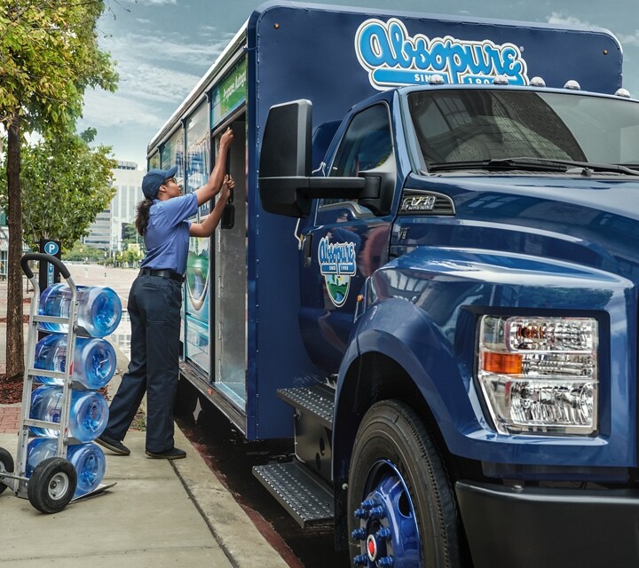 Primer plano de un trabajador descargando agua de una Ford F-750 Regular Cab 2024 con mejora para bebidas en una calle de ciudad