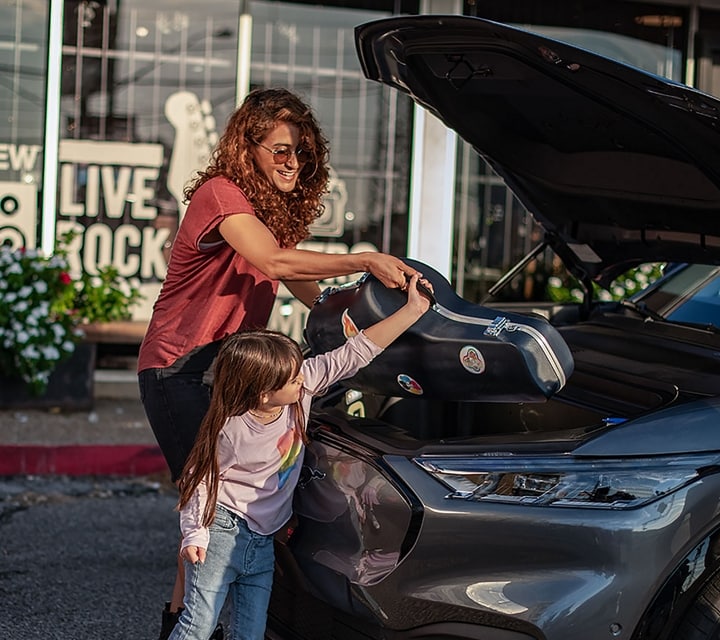 Una mujer ayuda a su hijo a colocar un instrumento musical en la cajuela delantera de una SUV Ford Mustang Mach-E 2023