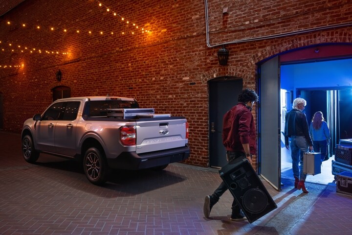 Una Ford Maverick® LARIAT 2023 en Iconic Silver estacionada en un callejón con músicos ingresando su equipo en un club nocturno