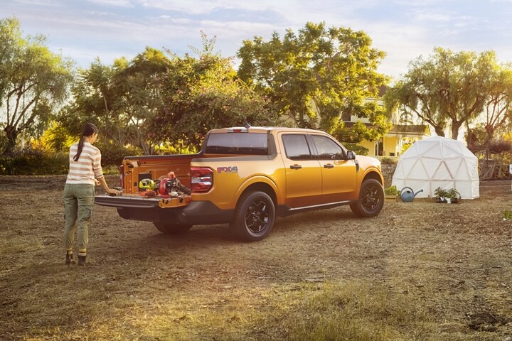 Una mujer en un jardín descarga plantas de la puerta trasera de múltiples posiciones de una Ford Maverick® XLT 2023 en Cyber Orange
