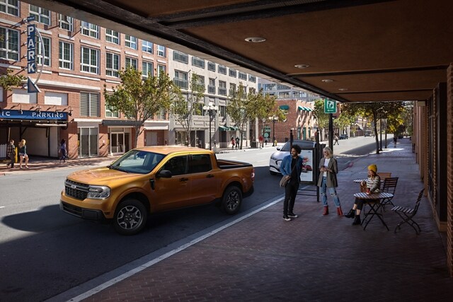Un modelo de la Ford Maverick® XLT 2023 en Cyber Orange con cámara de marcha atrás estacionando en paralelo fuera de un café