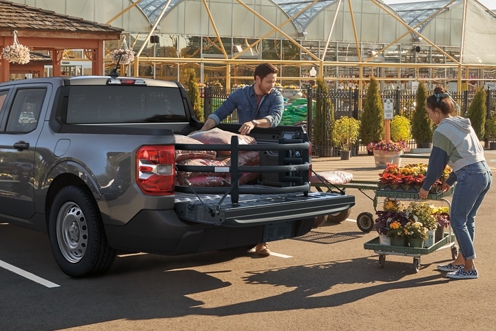 Dos personas poniendo flores y bolsas de tierra en la plataforma de una camioneta Ford Maverick® 2023 con extensión tipo jaula disponible