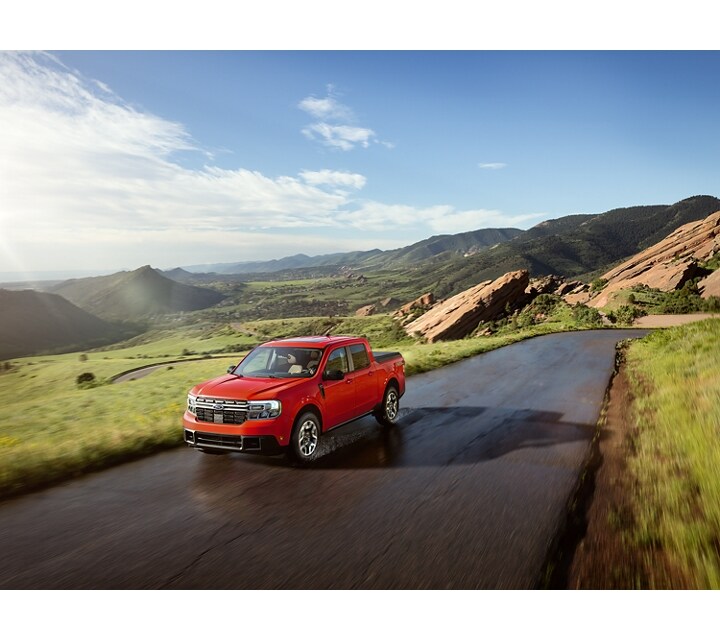 Una camioneta Ford Maverick® 2024 en Hot Pepper Red andando por una carretera en un lugar pintoresco con montañas al fondo