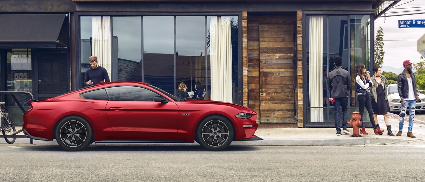Una Ford Mustang® Coupe 2023 estacionada cerca del frente de una tienda con una persona en primer plano