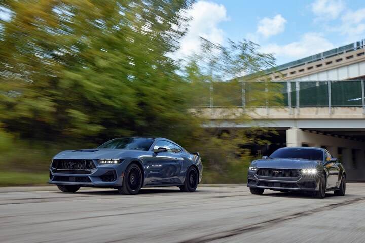Una Mustang® GT cupé 2024 en Vapor Blue Metallic y una cupé EcoBoost® en Carbonized Gray Metallic andando por una carretera