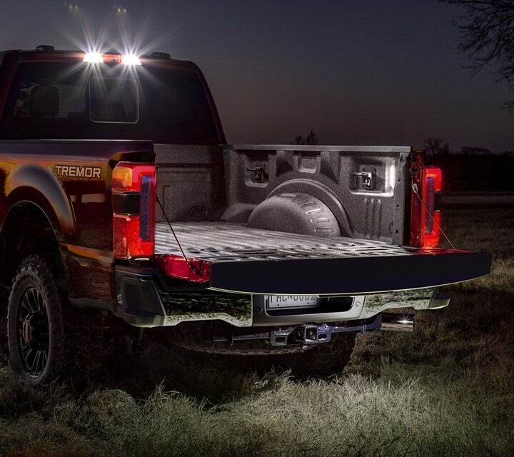 2024 Ford Super Duty® F-250® LARIAT® TREMOR® model parked in a field with its tailgate down and available LED lights lit
