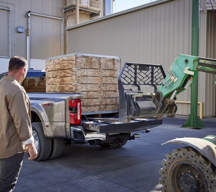 Man watching a hi-low loading a pallet into the bed of a 2024 Ford Super Duty® pickup