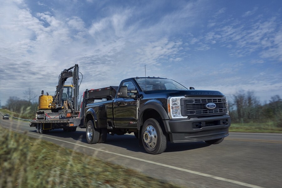 Una Ford Super Duty® F-450® XL2024 en Agate Black enganchada a un tráiler que transporta una retroexcavadora