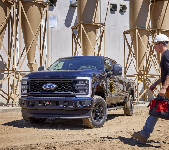 ​​​​​​​Un hombre pasando junto a una camioneta Ford Super Duty® 2024 estacionada cerca de un silo de granos