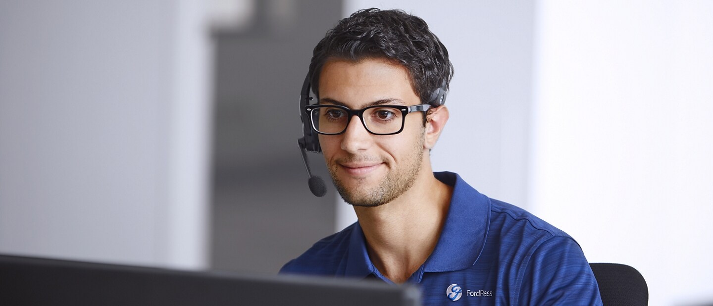 Hombre usando un auricular con micrófono sentado enfrente de la pantalla de una computadora