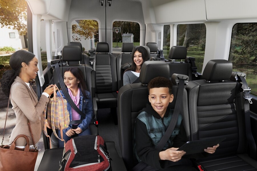 Interior de una van para pasajeros Transit® 2023 mostrando a una mamá entregando la mochila a su hija mientras los otros pasajeros esperan sentados
